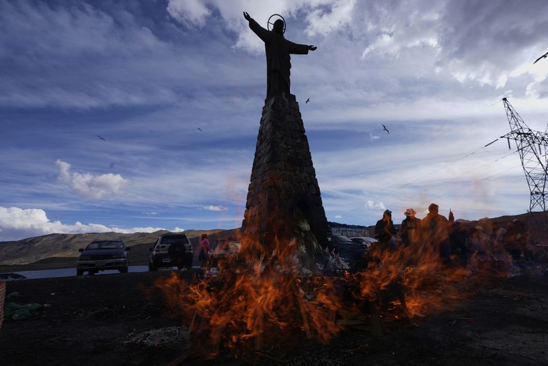Una estatua de Jesucristo se alza sobre personas que queman ofrendas en conmemoración del mes de la Pachamama, o Madre Tierra, cumpliendo una antigua tradición para pedir una buena cosecha, en La Cumbre, una montaña considerada sagrada en las afueras de La Paz, Bolivia, el viernes 1 de agosto de 2025. (Foto AP/Juan Karita)