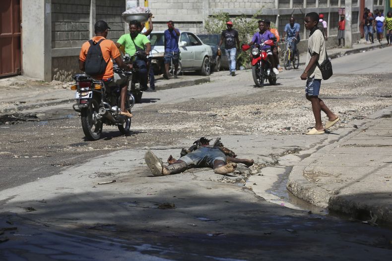 Transeúntes caminan junto a un cuerpo en descomposición abandonado en una calle del centro de Puerto Príncipe, Haití, el miércoles 13 de noviembre de 2024. (AP Foto/Odelyn Joseph)