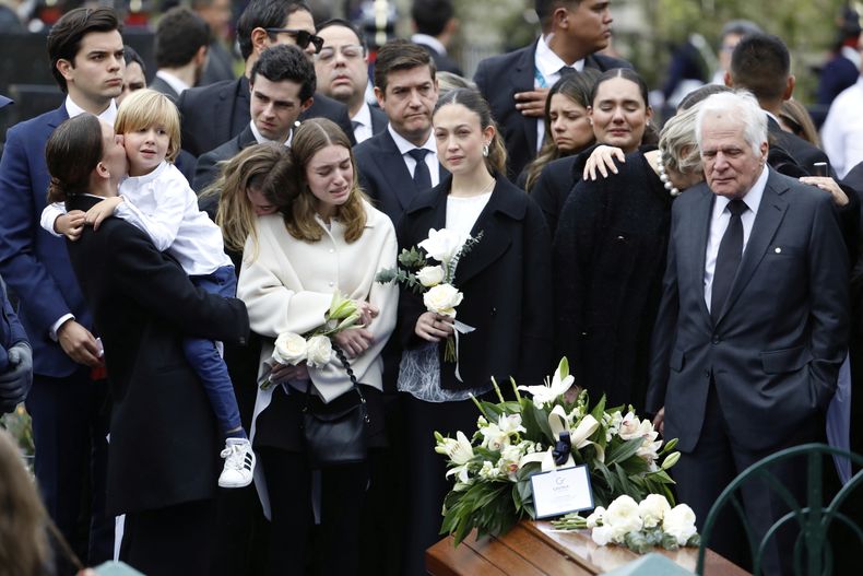 Miguel Uribe, a la derecha, y María Claudia Tarazona, con su hijo Alejandro en brazos, padre y esposa del aspirante presidencial y senador opositor Miguel Uribe, fallecido a causa de las heridas sufridas al recibir un disparo en un mitin político, se encuentran junto a otros familiares junto a su ataúd en el cementerio durante su funeral en Bogotá, Colombia, el miércoles 13 de agosto de 2025. (Foto AP/John Vizcaino)