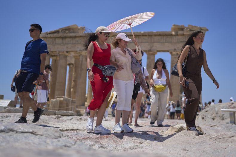 Turistas con un paraguas caminan ante el antiguo templo del Partenón en la Acrópolis, el jueves 26 de junio de 2025, durante la primera ola de calor del verano en Grecia, en la que se espera que las temperaturas superen los 40 grados Celsius (104 Farenheit).(AP Foto/Petros Giannakouris)