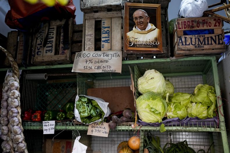 Una imagen del papa Francisco cuelga junto a un cartel que dice en español Pago con tarjeta 7% débito, 12% crédito, en un mercado de frutas y verduras en Buenos Aires, Argentina, el jueves 11 de mayo de 2023. Según un reciente Informe de Seguridad Alimentaria del Banco Mundial, Argentina ha visto una tasa de inflación anual del 107% en los precios de los alimentos. (Foto AP/Natacha Pisarenko)