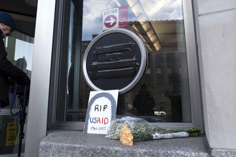 Flores y un letrero afuera de las oficinas de la Agencia de los Estados Unidos para el Desarrollo Internacional (USAID, por sus siglas en inglés), el viernes 7 de febrero de 2025, en Washington. (AP Foto/Jose Luis Magana)
