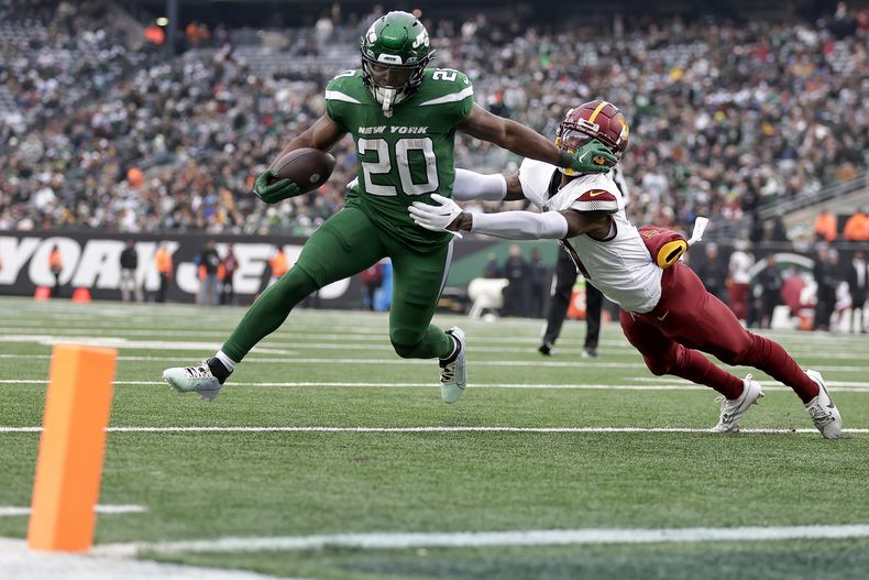 Breece Hall (20), running back de los Jets de Nueva York, se quita con el brazo al safety de los Commanders de Washington Kamren Curl (31) en su camino a la zona de anotación para un touchdown durante el segundo cuarto del partido de la NFL, el domingo 24 de diciembre de 2023, en East Rutherford, Nueva Jersey. (AP Foto/Adam Hunger)