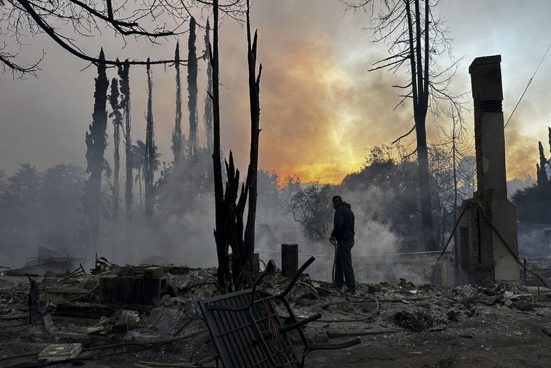 Un residente apaga pequeñas llamas en una propiedad arrasada por un incendio que azotó el vecindario de Pacific Palisades, en Los Ángeles, California, el miércoles 8 de enero de 2025. (AP Foto/Eugene Garcia)