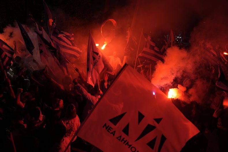 Simpatizantes de Kyriakos Mitsotakis, líder del partido de centro-derecha Nueva Democracia, sostienen bengalas frente a la sede del partido, el domingo 25 de junio de 2023, en Atenas, Grecia. (AP Foto/Petros Giannakouris)
