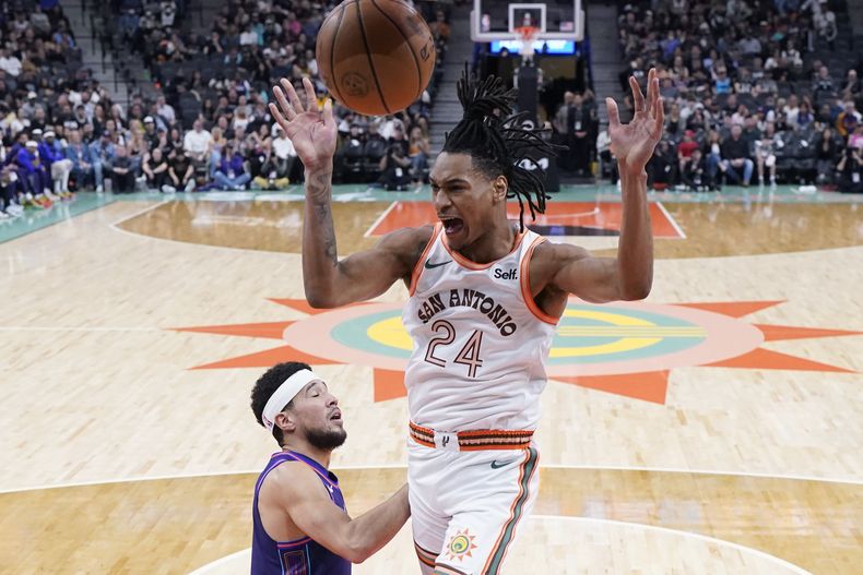 Devin Vassell (24), de los Spurs de San Antonio, anota sobre Devin Booker (1), de los Suns de Phoenix, durante la primera mitad del juego de baloncesto de la NBA, en San Antonio, el lunes 25 de marzo de 2024. (AP Foto/Eric Gay)