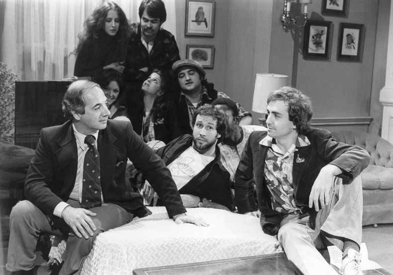 ARCHIVO - El secretario de prensa de la Casa Blanca, Ron Nessen, a la izquierda, aparece en el set de Saturday Night Live con el productor Lorne Michaels, a la derecha, y los miembros del elenco Chevy Chase, en primer plano al centro, Laraine Newman, al fondo a la izquierda, Dan Aykroyd, al fondo a la derecha, Jane Curtain, segunda fila de izquierda a derecha, Gilda Radner, John Belushi y Garret Morris, parcialmente visible, en abril (Foto AP)