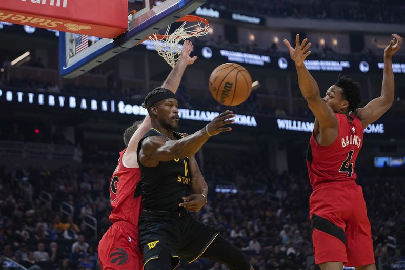 El alero de los Warriors de Golden State, Jimmy Butler III, centro, pasa el balón entre el pívot de los Raptors de Toronto, Jakob Poeltl, izquierda, y el escolta Scottie Barnes durante la primera mitad de un partido de baloncesto de la NBA, el jueves 20 de marzo de 2025, en San Francisco. (AP Foto/Godofredo A. Vásquez)