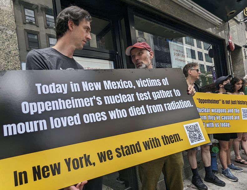 Matthew Bolton, a la izquierda, y Jan-Christoph Zoels, al centro, sostienen un cartel mientras se manifiestan en la ciudad de Nueva York el 15 de julio de 2023. Activistas se reunieron para llamar la atención hacia los residentes de Nuevo México que estuvieron expuestos a la radiación durante la prueba atómica Trinity realizada en 1945 como parte del Proyecto Manhattan. El mitin procedió a una proyección y un panel de discusión sobre la nueva película Oppenheimer. (Andrew Facini vía AP)