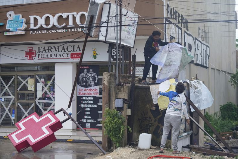 Residentes limpian la entrada de una farmacia dañada por el huracán Beryl, el viernes 5 de julio de 2024, en Tulum, México. (AP Foto/Fernando Llano)