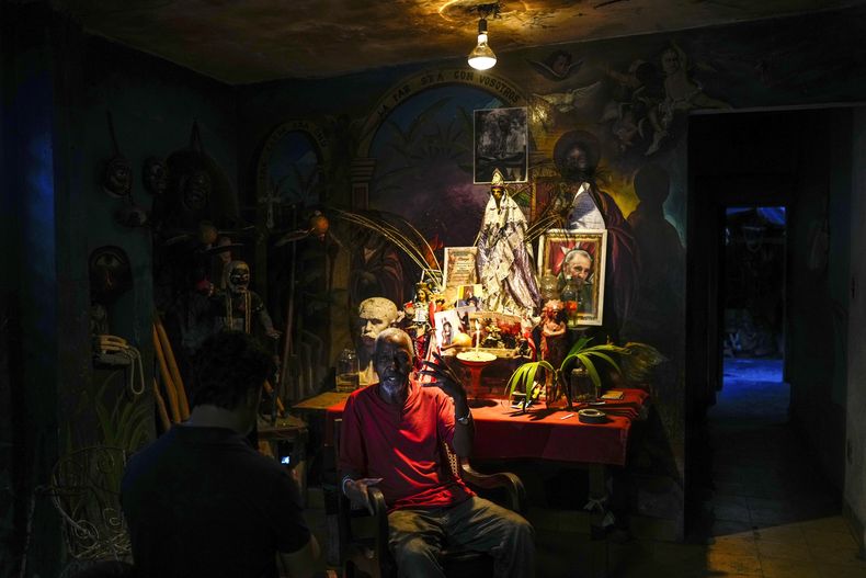 Juan González se sienta junto a un altar adornado con estatuillas de deidades de la santería afrocubana, incluida Oshún y una foto del fallecido líder cubano Fidel Castro, en su casa de El Cobre, Cuba, el sábado 10 de febrero de 2024. (AP Foto/Ramón Espinosa)