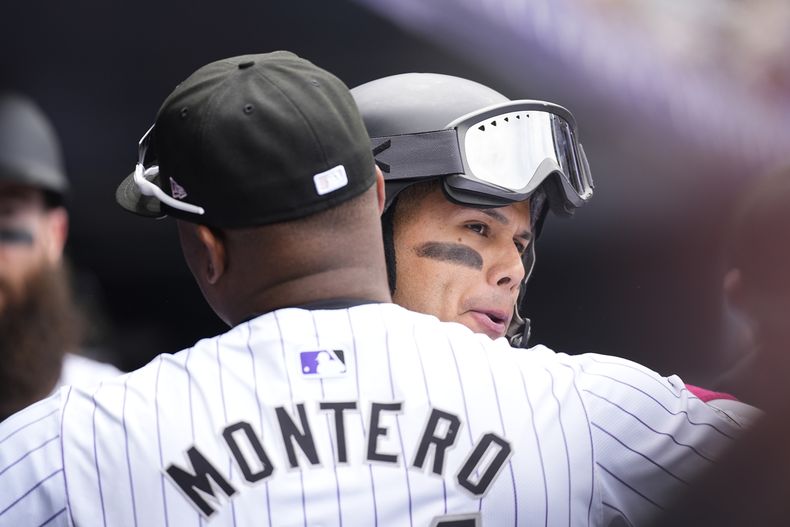 El dominicano de los Rockies de Colorado Elehuris Montero (izquierda) abraza al venezolano Ezequiel Tovar (derecha) al regresar a la banca luego de impactar un jonrón de dos carreras ante los Rangers de Texas en la primera entrada del juego de béisbol, el domingo 12 de mayo de 2024, en Denver. (AP Foto/David Zalubowski)