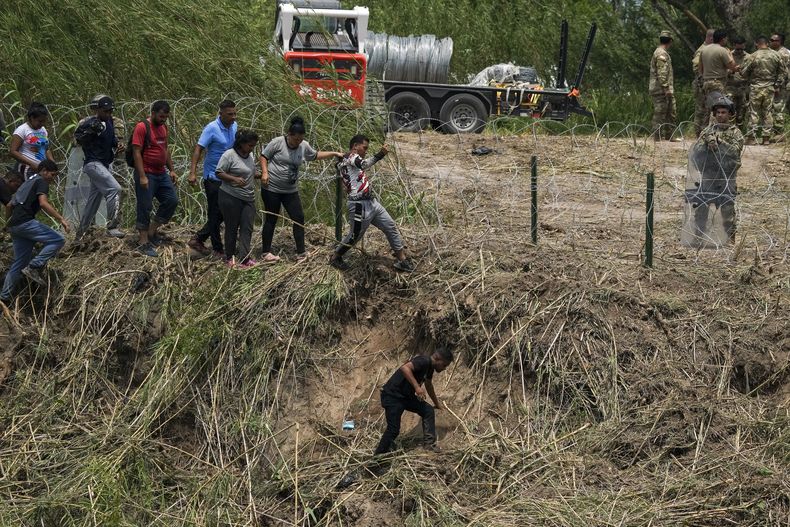 Un elemento de la Guardia Nacional de Texas permanece detrás de alambre de púas mientras migrantes intentan ingresar a Estados Unidos en la margen del río Bravo (Rio Grande en inglés), en una imagen captada el jueves 11 de mayo de 2023 desde Matamoros, México. Gran cantidad de migrantes se apresuraban a cruzar la frontera entre ambos países con la esperanza de entrar a Estados Unidos horas antes de que se suspendan las restricciones al asilo relacionadas con la pandemia de COVID-19. (AP Foto/Fernando Llano)