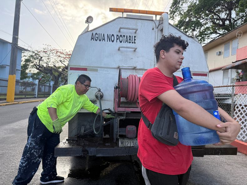 Bryan Pérez carga con una garrafa de agua para su departamento en el complejo de viviendas públicas Villa Kennedy, en San Juan, Puerto Rico, el 10 de junio de 2026. (AP Foto/Dánica Coto)