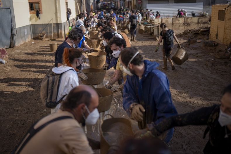 Voluntarios hacen una cadena humana para sacar barro en cubos, en una zona todavía enlodada tras las letales inundaciones en Masanasa, Valencia, el 7 de noviembre de 2024. (AP Foto/Emilio Morenatti)