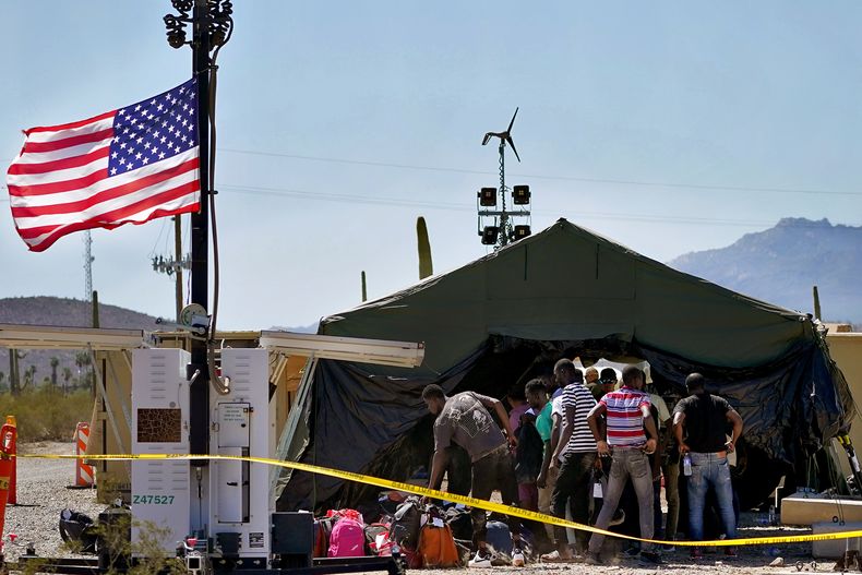 Un grupo de hombres detenidos por agentes de la Patrulla Fronteriza luego de cruzar el muro fronterizo en el Sector de Tucson de la frontera Estados Unidos-México, se quita las mochilas antes de ser procesado en un centro improvisado de recepción en el Monumento Nacional Organ Pipe Cactus cerca de Lukeville, Arizona, el martes 29 de agosto de 2023. (AP Photo/Matt York)
