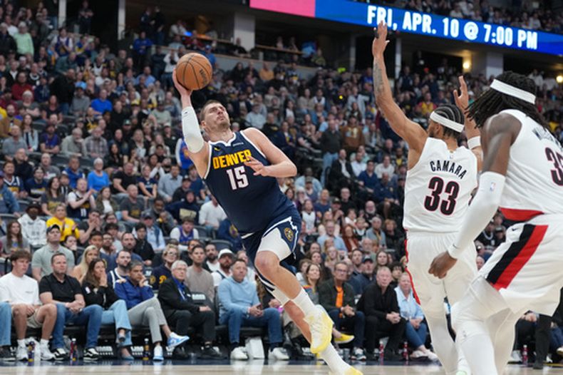 El pívot de los Nuggets de Denver Nikola Jokić intenta lanzar el balón tras recibir una falta de Toumani Camara de los Trail Blazers de Portland junto al pívot Robert Williams III en el encuentro del lunes 6 de abril del 2026. (AP Foto/David Zalubowski)