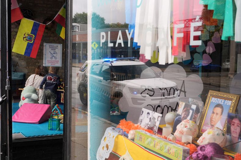 Una patrulla de la policía de Chicago aparece reflejada en la ventana del Luna y Cielo Play Cafe, donde se exhibe una foto enmarcada de Silverio Villegas González, un mexicano abatido por un agente de migración, en el barrio de Logan Square de Chicago, el 15 de octubre de 2025. (Foto AP/Rebecca Blackwell, Archivo)