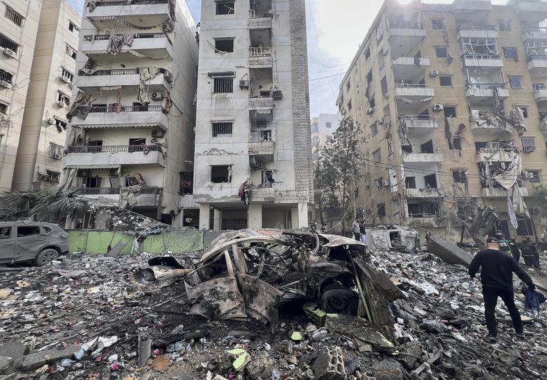 Un hombre camina junto a un coche destruido y edificios dañados en el lugar que fue alcanzado por un ataque aéreo israelí en Dahiyeh, en el suburbio sur de Beirut, Líbano, viernes 28 de marzo de 2025. (AP foto/Hussein Malla)