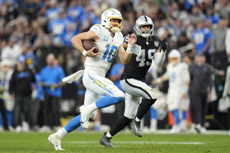Justin Herbert (10), quarterback de los Chargers de Los Ángeles, corre con el balón, con Charles Snowden (49), de los Raiders de Las Vegas, persiguiéndolo durante la segunda mitad del partido de la NFL, el domingo 5 de enero de 2025, en Las Vegas. (AP Foto/Abbie Parr)