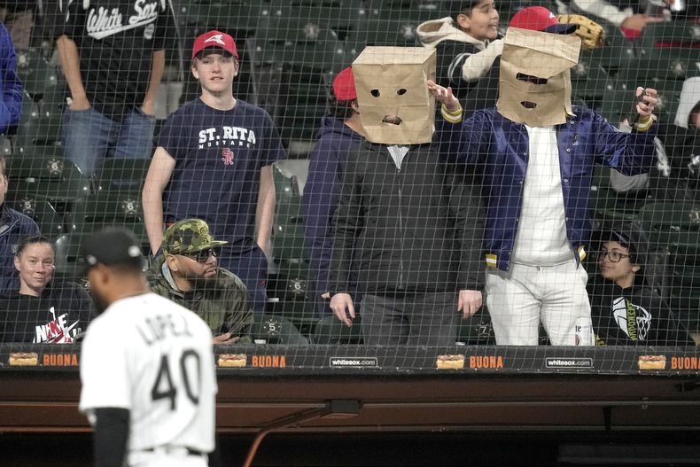 Aficionados se cubren sus cabezas con bolsas de papel durante el juego de los Medias Blancas de Chicago contra los Rays de Tampa Bay, el jueves 27 de abril de 2023, en Chicago. (AP Foto/Charles Rex Arbogast)