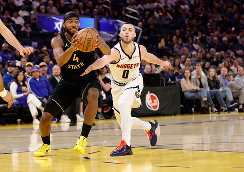 Moses Moody (4), de los Warriors de Golden State, controla el balón ante la presión defensiva de Christian Braun (0), de los Nuggets de Denver, durante la primera mitad del juego de baloncesto de la NBA, el domingo 22 de febrero de 2026, en San Francisco. (AP Foto/Kelley L Cox)