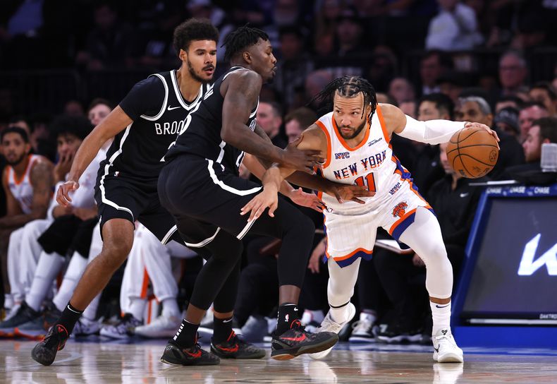 El escolta de los Knicks de Nueva York, Jalen Brunson (11), conduce hacia la canasta contra el alero de los Nets de Brooklyn, Dorian Finney-Smith, segundo desde la izquierda, y Cam Johnson, a la izquierda, durante la primera mitad, el domingo 17 de noviembre de 2024, en Nueva York. (AP Foto/Noah K. Murray)