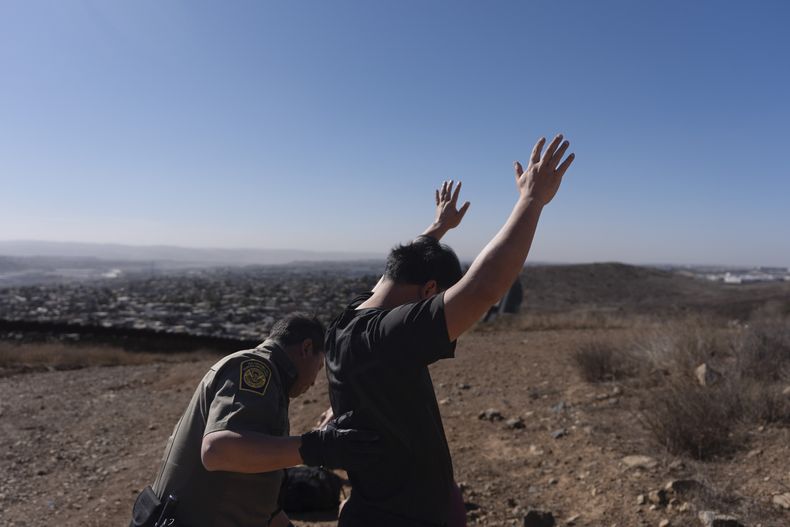Un agente de la Patrulla Fronteriza revisa a un hombre luego que un grupo de cuatro individuos cruzó la frontera de manera ilegal a través de un espacio entre dos muros que separan a México de Estados Unidos y se entregó a las autoridades estadounidenses, el jueves 23 de enero de 2025, en San Diego. (AP Foto/Gregory Bull)