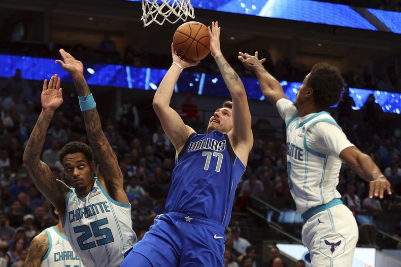 Luka Doncic (77), de los Mavericks de Dallas, dispara ante la presión de P.J. Washington (25) y Theo Maledon, derecha, de los Hornets de Charlotte, en la segunda mitad del juego de baloncesto de la NBA, el domingo 5 de noviembre de 2023, en Dallas. (AP Foto/Richard W. Rodriguez)