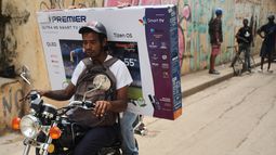 Un motociclista transporta a un cliente con un televisor en una caja durante un apagón en La Habana, el martes 17 de marzo de 2026. (AP Foto/Ramón Espinosa)