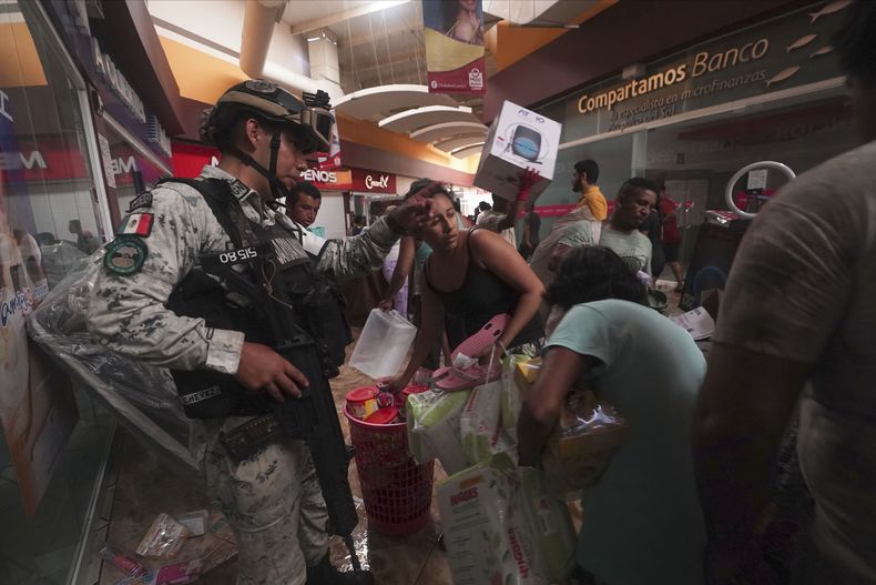 Un militar de la Guardia Nacional mexicana intenta impedir que personas se lleven productos de las tiendas de un centro comercial tras el devastador paso del huracán Otis por Acapulco, México, el miércoles 25 de octubre de 2023. El huracán Otis provocó grandes destrozos al atravesar la costa sur del Pacífico mexicano con categoría 5, al llegar con grandes inundaciones, quebrar carreteras y dejar sin servicio eléctrico y telefónico a grandes partes del estado de Guerrero. (AP Foto/Marco Ugarte)