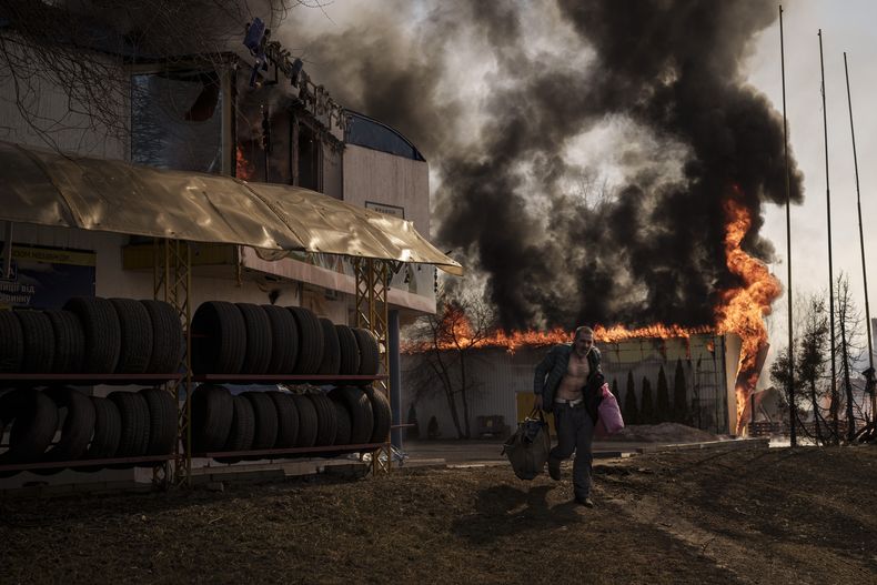 Un hombre corre tras recuperar artículos de una tienda en llamas después de un ataque ruso en Járkiv, Ucrania, el viernes 25 de marzo de 2022. (AP Foto/ Felipe Dana)