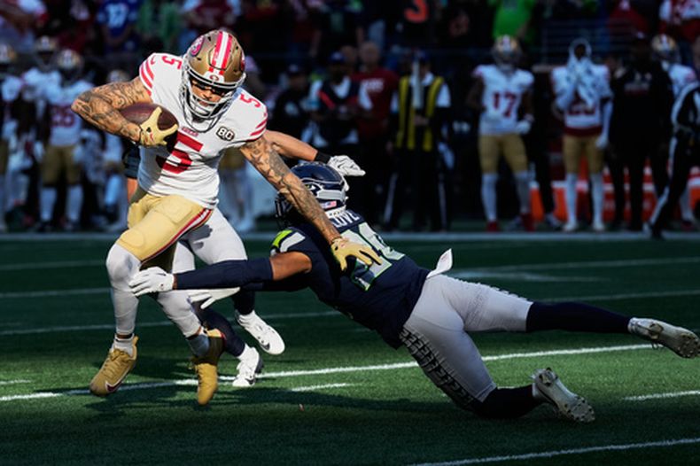 Mike Evans (5), receptor abierto de San Francisco, atrapa un pase y corre para evitar ser derribado por Julian Love (20), safety de Seattla, durante la segunda mitad del partido de la NFL, el domingo 11 de octubre de 2026, en Seattle. (AP Foto/Stephen Brashear)