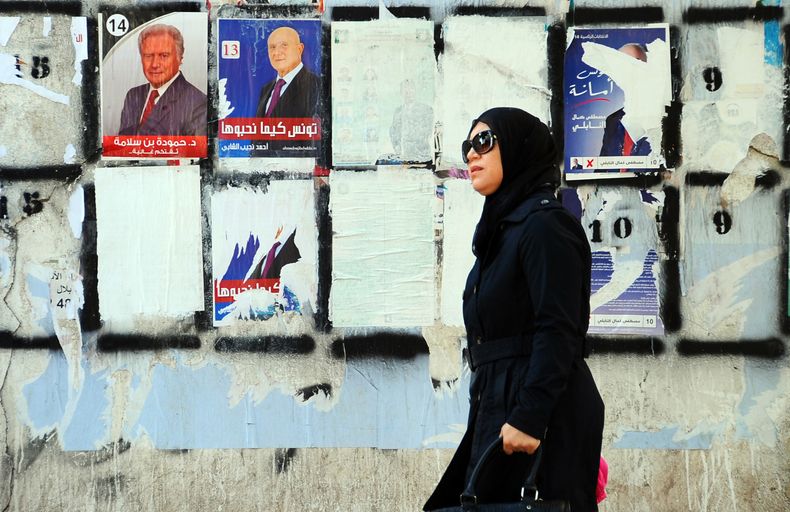 Una mujer pasa caminando junto a un muro empapelado con carteles electorales dos d&iacute;as antes de la primera vuelta de las elecciones presidenciales en T&uacute;nez, el 21 de noviembre de 2014. (Foto AP/Hassene Dridi)