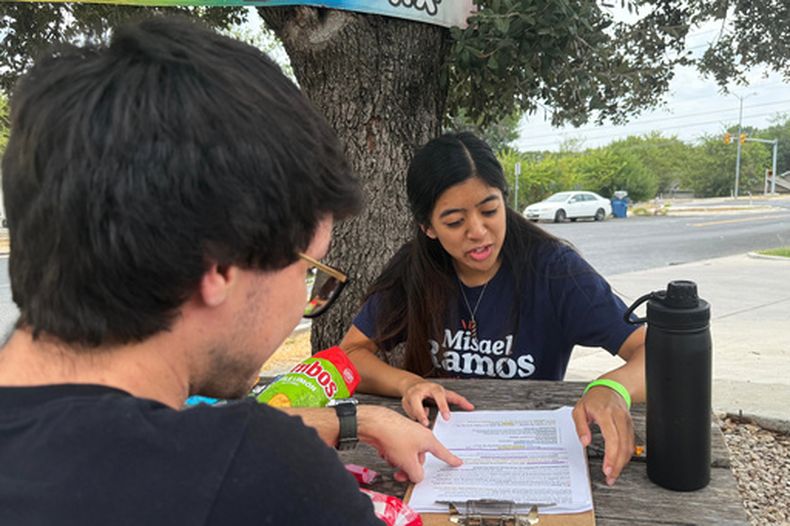 Esta fotografía, tomada con un teléfono inteligente, muestra a dos miembros de los Socialistas Democráticos de Estados Unidos, Mark Ramirez y Clarisse Manuel, durante una jornada de contacto con los votantes el sábado 26 de septiembre de 2026, en Austin, Texas. (AP Foto/Jesse Bedayn)
