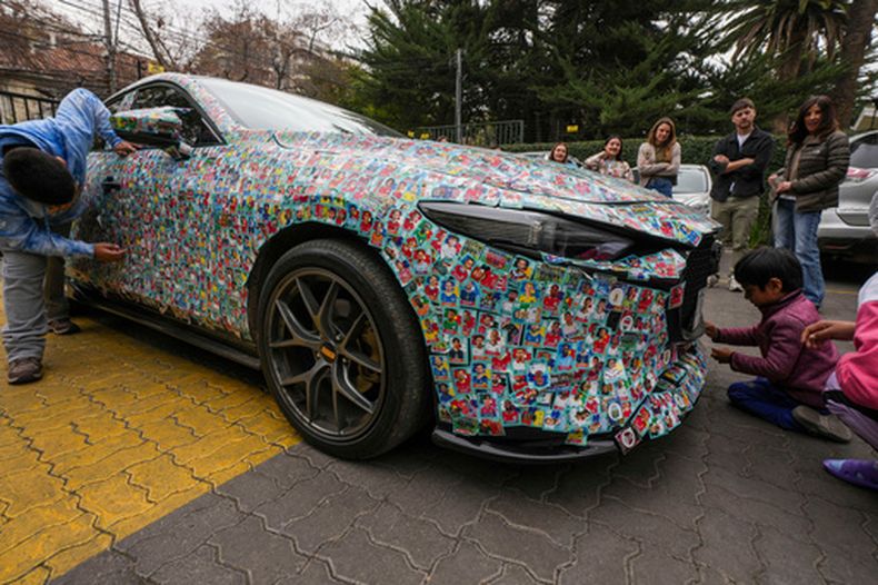 El auto del influencer chileno Ariel Osses se detiene en el estacionamiento de un hogar para niños con cáncer para que los pequeños puedan pegar más calcomanías de álbumes de fútbol del Mundial, que él les proporciona, en el exterior del vehículo, en Santiago de Chile, el miércoles 8 de julio de 2026. (Foto AP/Esteban Félix)