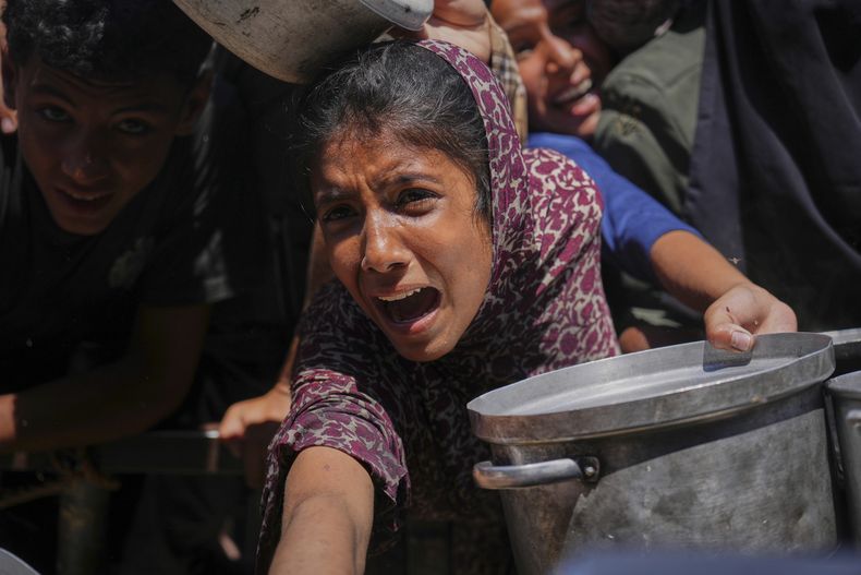 Palestinos tratan de recibir alimentos cocinados distribuidos en una cocina comunitaria en el área de Muwasi de Jan Yunis, en la Franja de Gaza, el viernes 23 de mayo de 2025. (AP Foto/Abdel Kareem Hana)