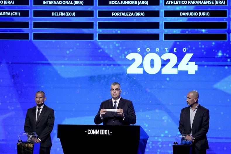 Frederico Nantes, centro, director de competencia de CONMEBOL, sostiene el papel que lleva el nombre de Universidad Católica de Ecuador durante el sorteo de la Copa Sudamericana, en Luque, Paraguay, el lunes 18 de marzo de 2024. (AP Foto/Jorge Saenz)