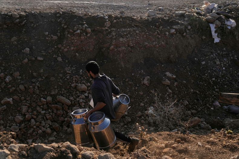 Un campesino palestino carga jarras de leche de su ganado atravesando una zanja cavada por el ejército israelí en una carretera al pueblo de Khirbet Ras al-Ahmar, al suereste de Tubas, en Cisjordania, para llevarla a vender el sábado 19 de septiembre de 2026. (AP Foto/Majdi Mohammed)