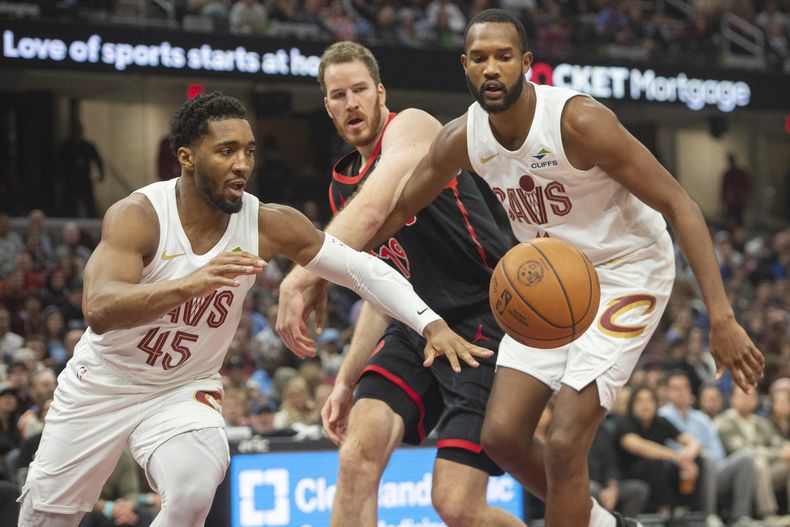 Donovan Mitchell (45), de los Cavaliers de Cleveland, Jakob Poeltl, centro, y Evan Mobley, a la derecha, de los Raptors de Toronto, van por un balón suelto durante la primera mitad de un partido en Cleveland, el domingo 24 de noviembre de 2024. (AP Foto/Phil Long)