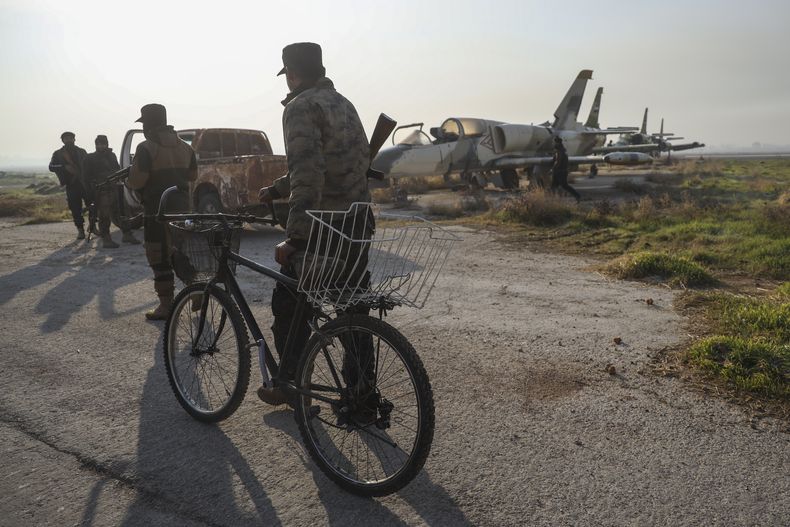 Combatientes de la oposición siria, junto a viejos aviones militares en el aeropuerto militar de Al-Nayrab tras hacerse con el control de las instalaciones, a las afueras de Alepo, el 2 de diciembre de 2024. (AP Foto/Omar Albam)