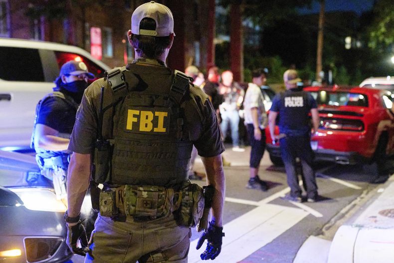 Oficiales de varias agencias federales, incluidos el FBI y la Policía de Parques, interrogan a una pareja que estaba comiendo afuera de un estacionamiento, el martes 12 de agosto de 2025, en el noroeste de Washington, cerca de Kennedy St. NW. La pareja fue liberada después que les registraron el automóvil. (AP Foto/Jacquelyn Martin)