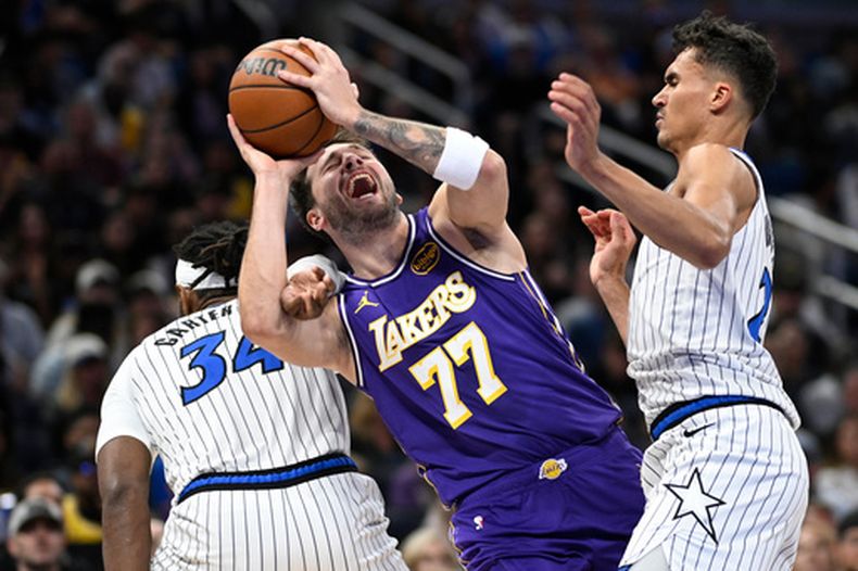 Luka Doncic (77), de los Lakers de Los Ángeles, recibe una falta de parte de Wendell Carter Jr. (34), del Magic de Orlando, mientras Tristan da Silva, derecha, llega a apoyar en la marca defensiva, durante la primera mitad del juego e baloncesto de la NBA del sábado 21 de marzo de 2026, en Orlando, Florida. (AP Foto/Phelan M. Ebenhack)