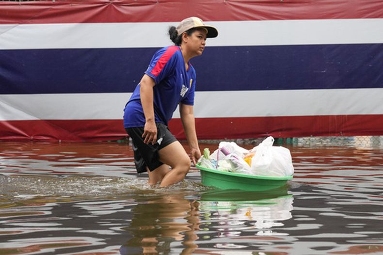 Una mujer vadea zonas inundadas ante una bandera nacional tras fuertes lluvias en Bangkok, Tailandia, el domingo 27 de septiembre de 2026. (AP Foto/Sakchai Lalit)