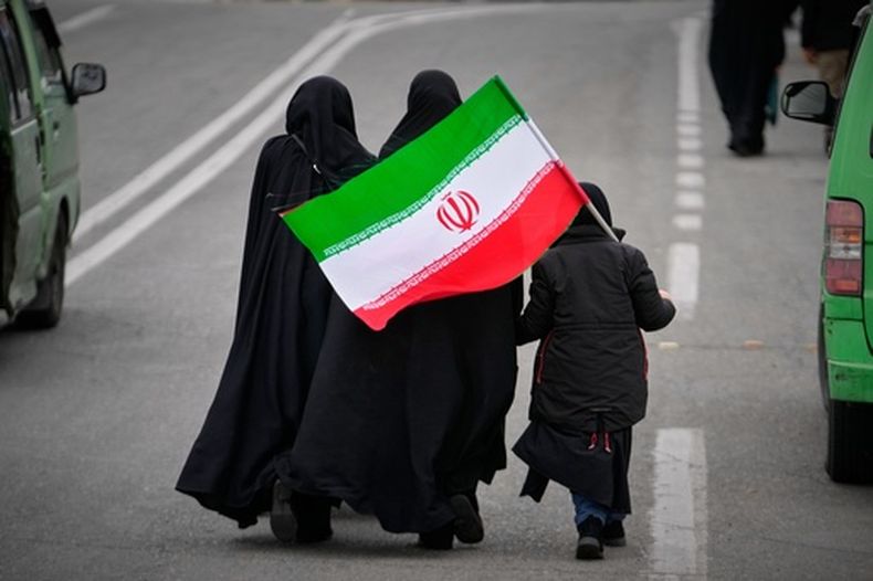 Dos mujeres y una menor con una bandera iraní caminan hacia la Gran Mezquita para asistir a las oraciones del viernes en Teherán, Irán, el viernes 20 de marzo de 2026. (AP Foto/Vahid Salemi)