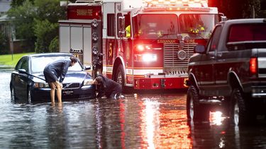 Dos personas atan un cabo a un auto varado en una calle anegada debido a las fuertes lluvias de la tormenta tropical Debby, el 5 de agosto de 2024, en Savannah, Georgia. (AP Foto/Stephen B. Morton)