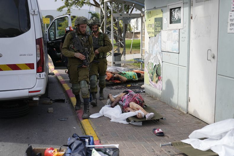 Soldados israelíes pasan junto a civiles asesinados por insurgentes de Hamás en Sderot, Israel, el 7 de octubre de 2023. Insurgentes de Hamás en la Franja de Gaza se infiltraron en el sur de Israel y dispararon miles de proyectiles al país mientras Israel comenzaba a atacar objetivos en el enclave palestino en respuesta. (AP Foto/Ohad Zwigenberg)