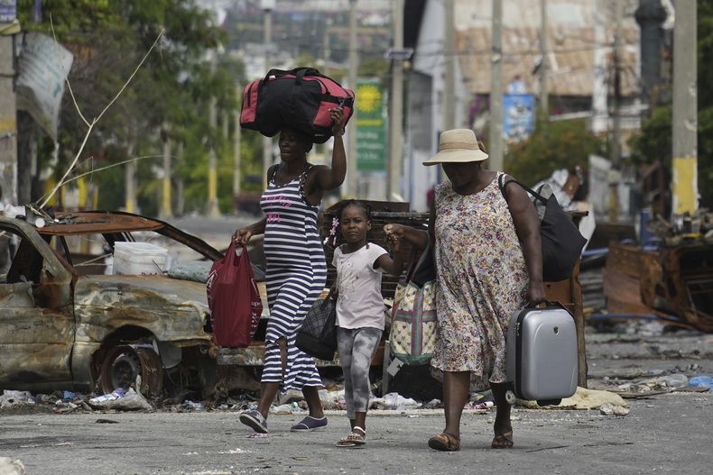 ARCHIVO - Residentes pasan junto a un automóvil quemado que bloquea la calle mientras evacuan el vecindario Delmas 22 para escapar de la violencia de las pandillas en Puerto Príncipe, Haití, el 2 de mayo de 2024. (AP Foto/Ramón Espinosa, Archivo)