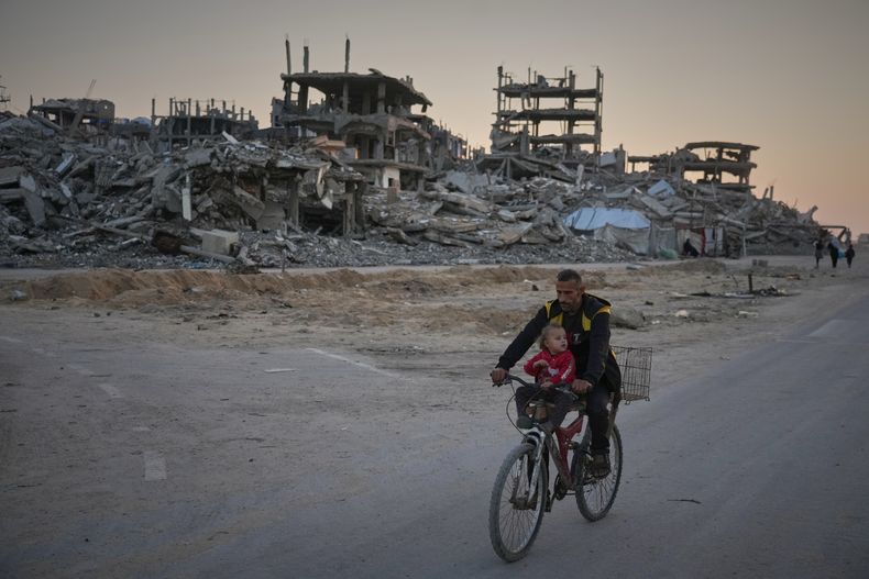 Un hombre carga a un niño mientras conduce su bicicleta por una calle destruida en el campamento de Al-Shati, en la Ciudad de Gaza, el martes 18 de noviembre de 2025. (AP Foto/Jehad Alshrafi)