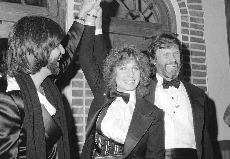 ARCHIVO - De izquierda a derecha, el productor Jon Peters, Barbra Streisand y Kris Kristofferson sonríen en un preestreno de la película A Star is Born, el 23 de diciembre de 1976, en Nueva York. (AP Foto/Suzanne Vlamis, Archivo)